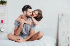 117877809-adult-couple-hugging-and-sitting-on-bed-with-white-bedding.webp